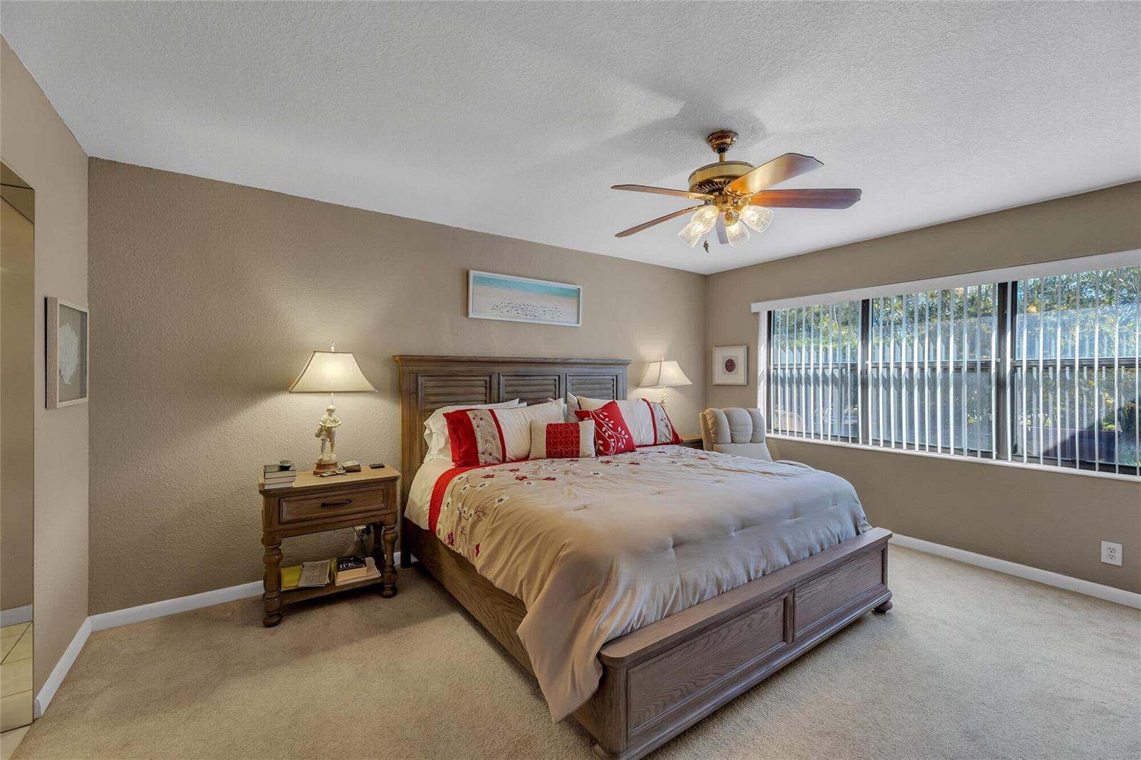 A bedroom features a wooden bed frame, a ceiling fan, and a large window with blinds — 2260 Seagrape Circle, Coconut Creek FL 33066, COCONUT CREEK, FL