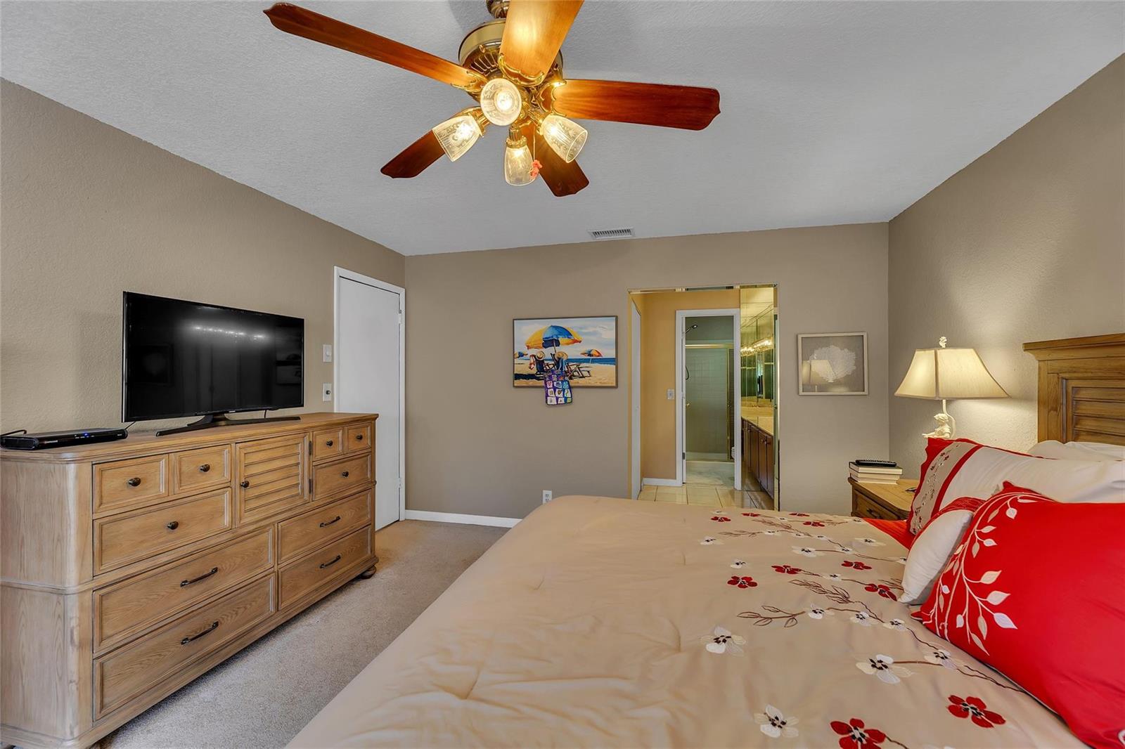 A bedroom features a wooden dresser, a ceiling fan, and a bed with red pillows — 2260 Seagrape Circle, Coconut Creek FL 33066, COCONUT CREEK, FL