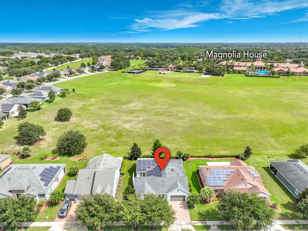 An aerial view shows a residential house with solar panels and a large grassy field — 107 BALMY COAST ROAD, GROVELAND, FL