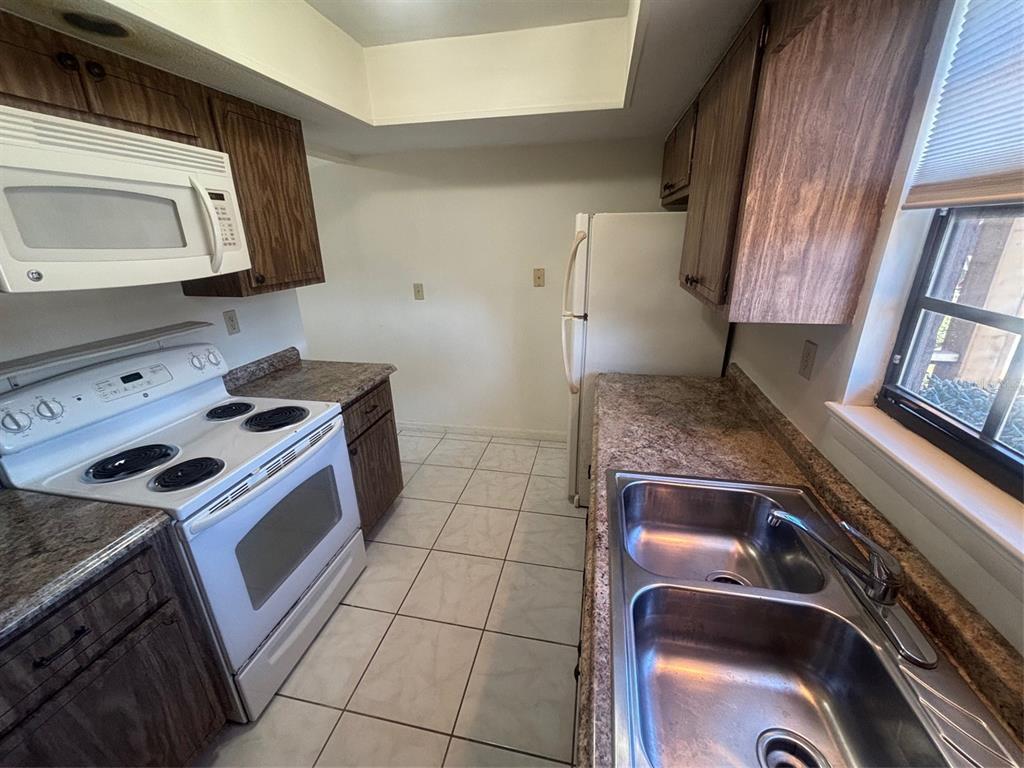 A kitchen features wood cabinets, white appliances, a double sink, and light-colored floor tiles — 500 NEWELL HILL ROAD UNIT 101A, LEESBURG, FL