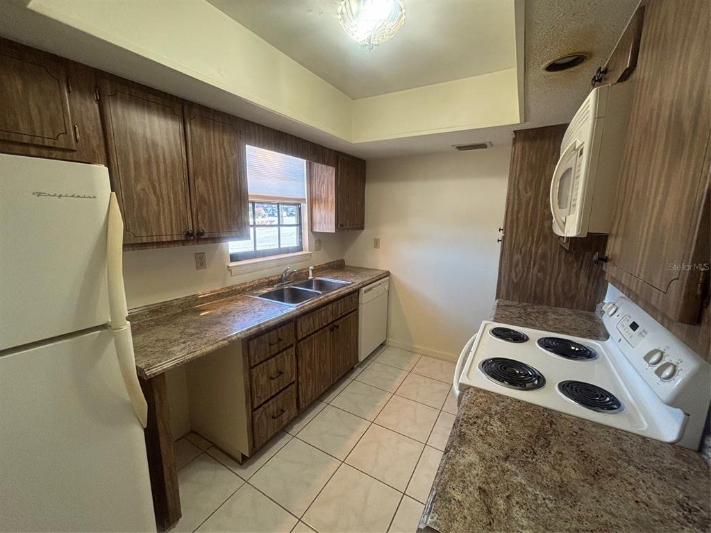 A kitchen features wood cabinets, laminate countertops, a white refrigerator, and a white electric stove — 500 NEWELL HILL ROAD UNIT 101A, LEESBURG, FL