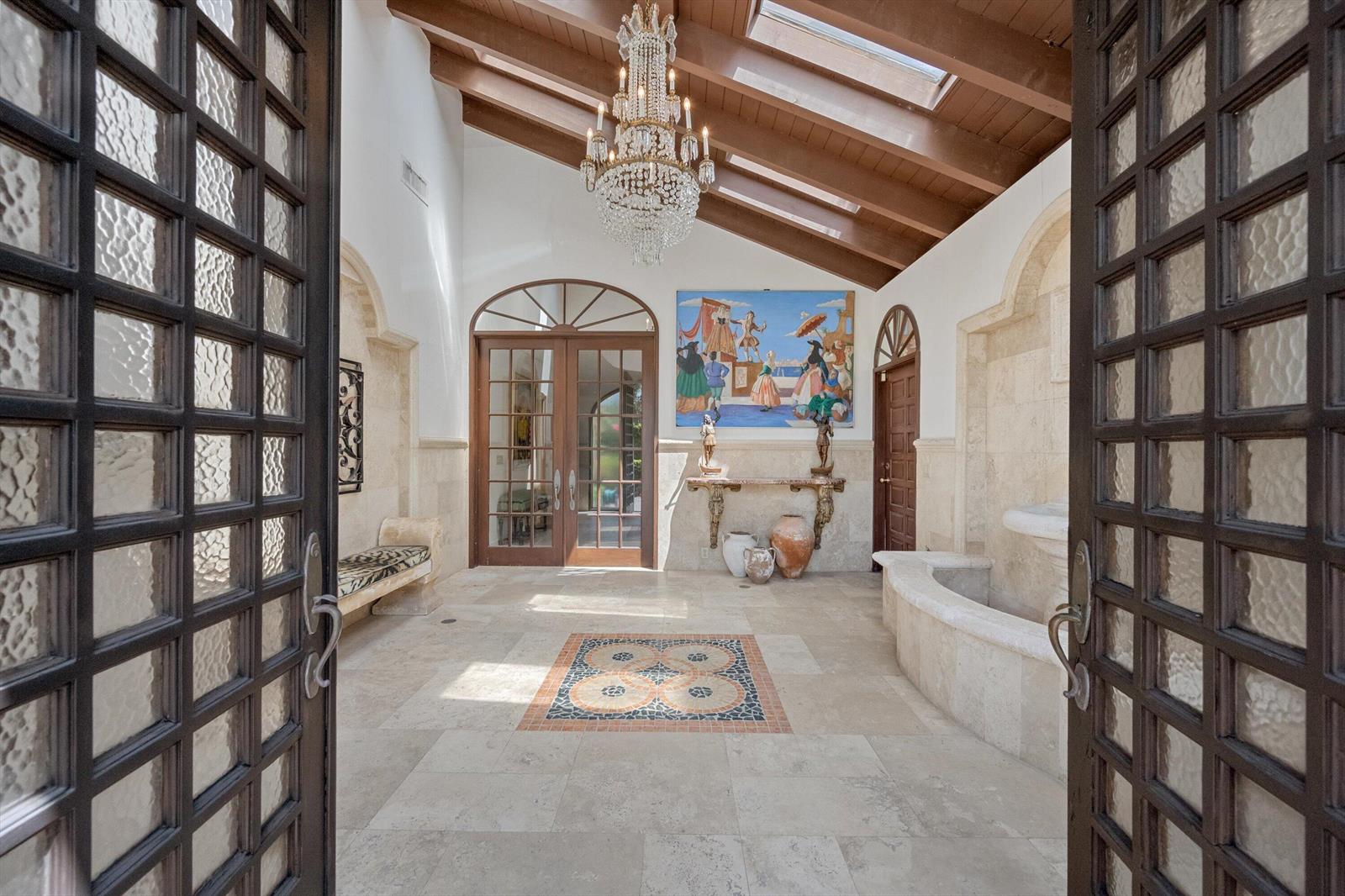 A sunlit foyer features a stone fountain, a crystal chandelier, and a mosaic floor inlay — 23 Sloans Curve Drive, Palm Beach FL 33480, PALM BEACH, FL