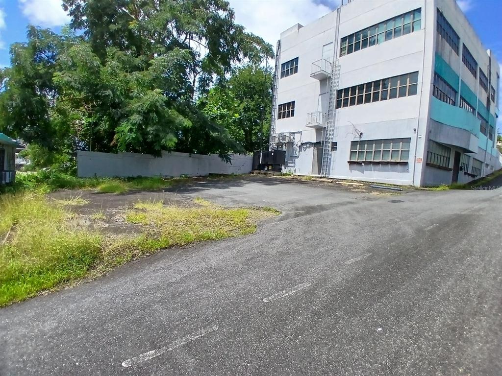 An asphalt parking lot sits beside a multi-story industrial building with a metal fire escape — 97 STATE ROAD 2 PUEBLO VIEJO, GUAYNABO, PR
