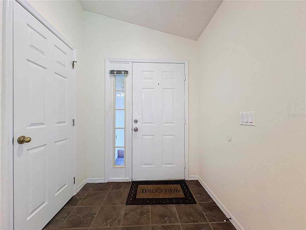 An entryway features a white front door with a sidelight, tiled flooring, and white walls — 2393 PAULETTE DRIVE, HAINES CITY, FL