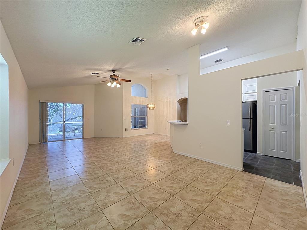 An open-concept living and dining area features beige tile flooring, vaulted ceilings, and sliding doors — 2393 PAULETTE DRIVE, HAINES CITY, FL