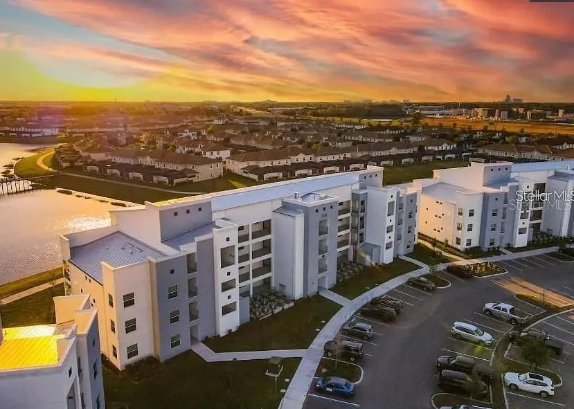 An aerial view of a multi-story apartment complex with a parking lot at sunset — 4741 CLOCK TOWER DRIVE UNIT 108, KISSIMMEE, FL