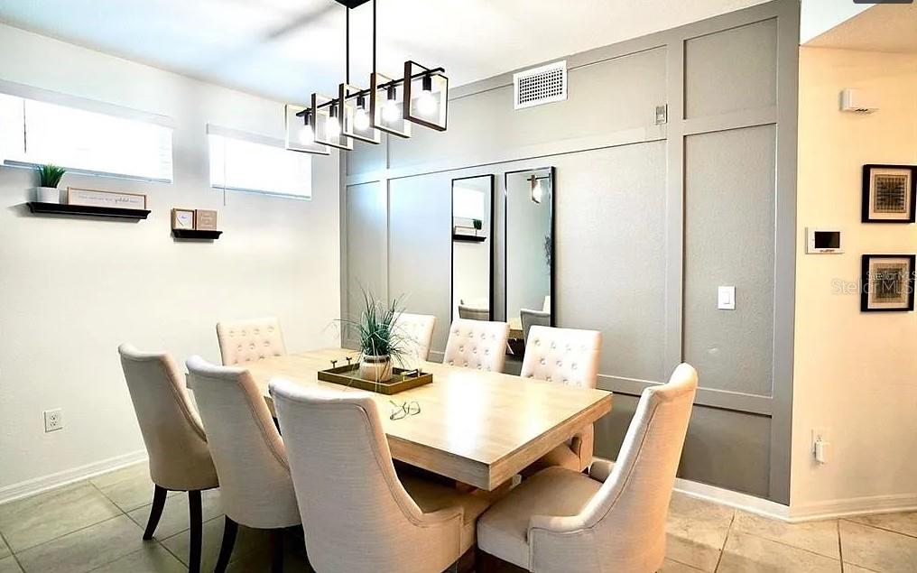 A dining room features a light wood table, upholstered chairs, and a gray paneled accent wall — 4741 CLOCK TOWER DRIVE UNIT 108, KISSIMMEE, FL