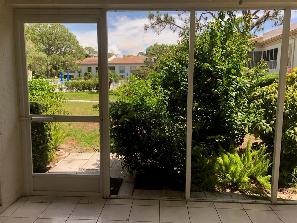 A view from a tiled screened-in porch looking out toward a grassy area and buildings — 5226 MARSH FIELD LANE UNIT 11, SARASOTA, FL