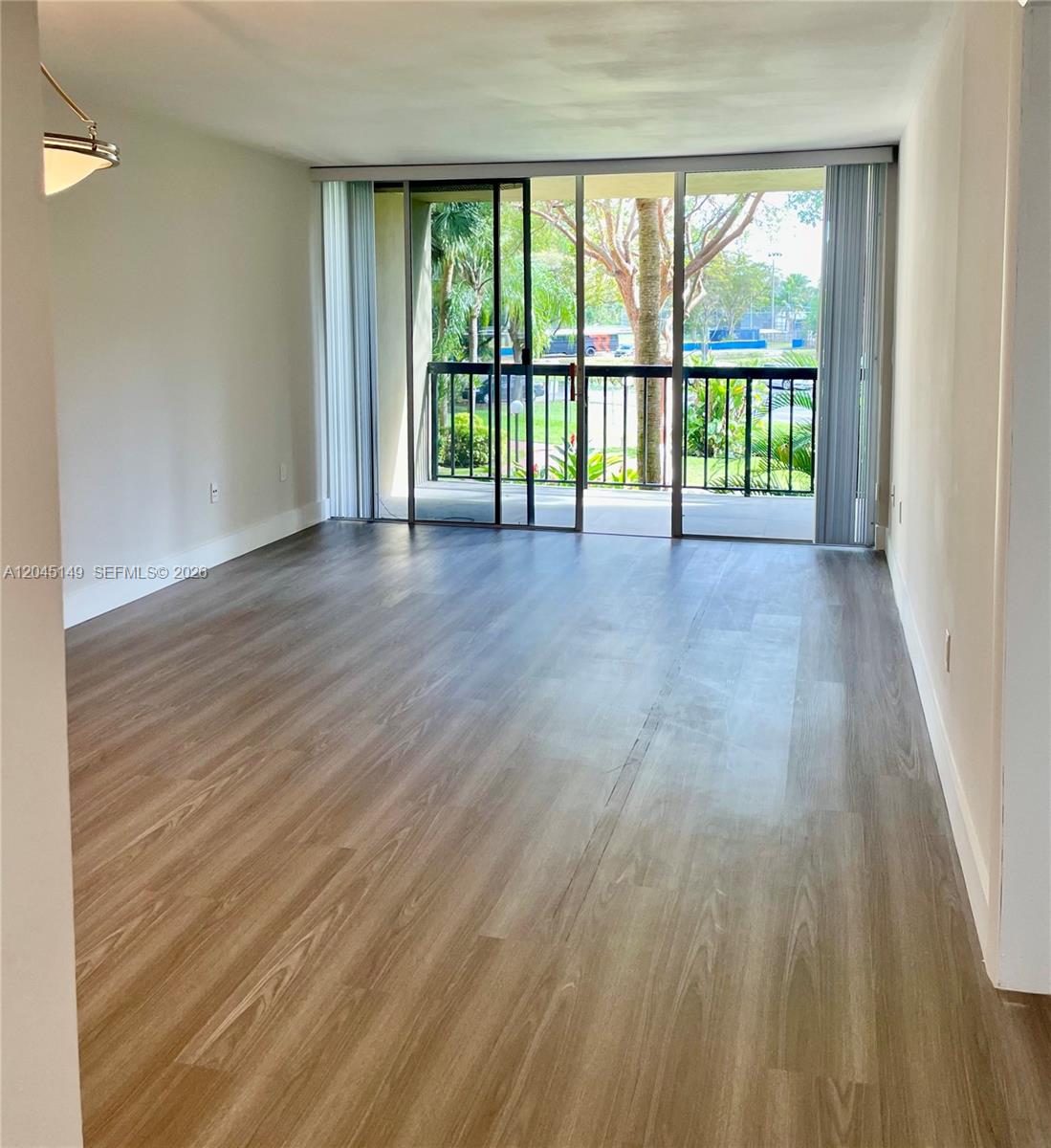 An empty living room features wood-look flooring, light walls, and a sliding glass door balcony — 10835 SW 112th Ave # 212, Miami FL 33176, MIAMI, FL