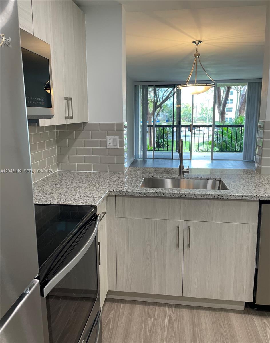 A kitchen with light wood cabinets, granite countertops, and a view of a balcony — 10835 SW 112th Ave # 212, Miami FL 33176, MIAMI, FL