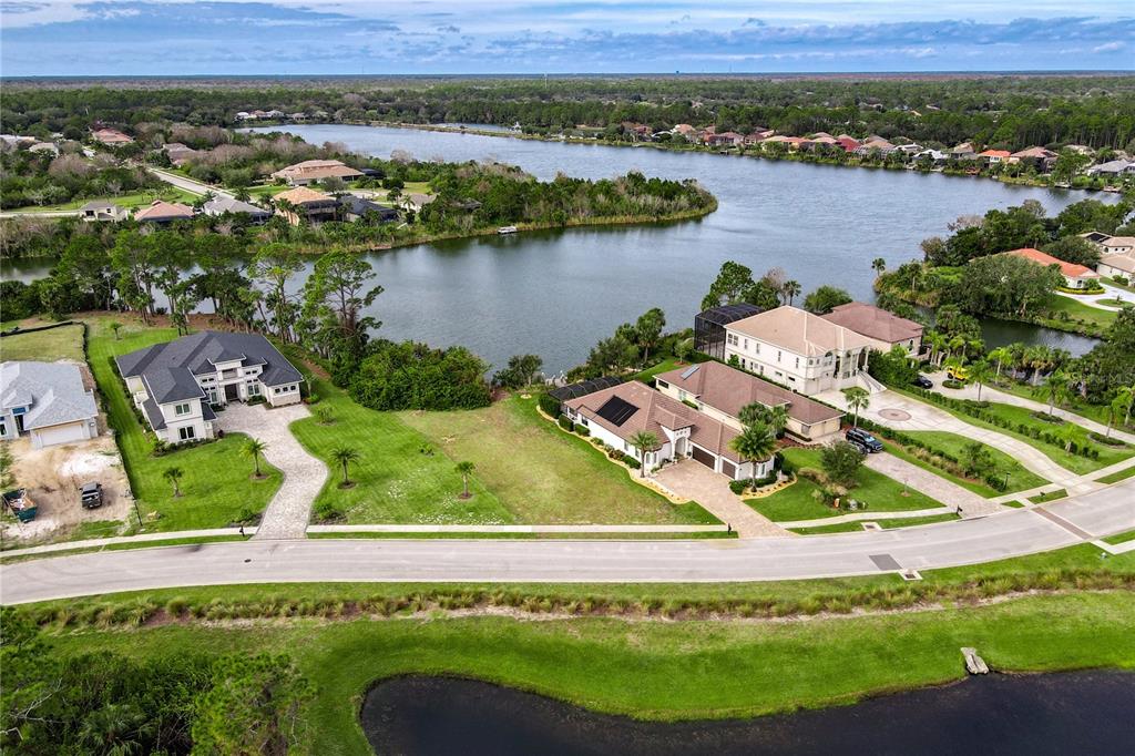 An aerial view shows two large houses with paved driveways situated along a lakefront — 22 HERON DRIVE, PALM COAST, FL