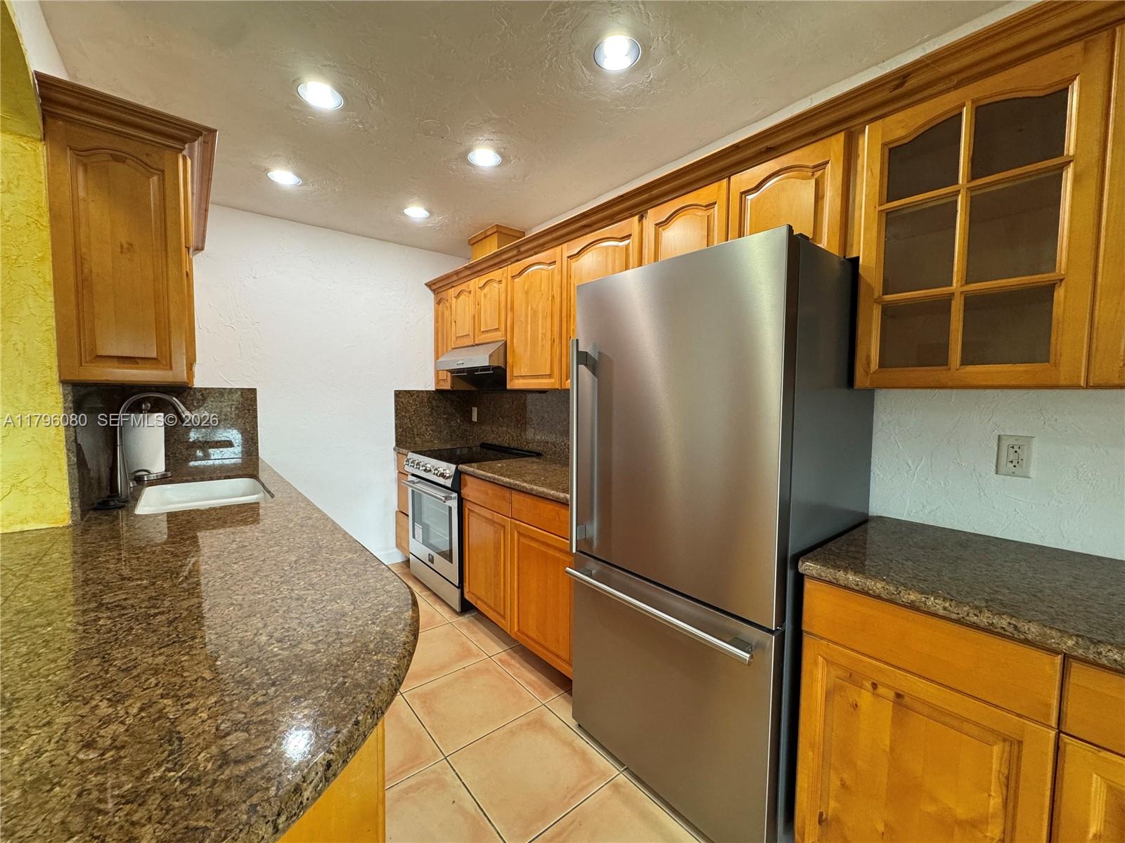 A kitchen features wood cabinets, granite countertops, stainless steel appliances, and tile flooring — 1700 Pierce St # 202, Hollywood FL 33020, HOLLYWOOD, FL