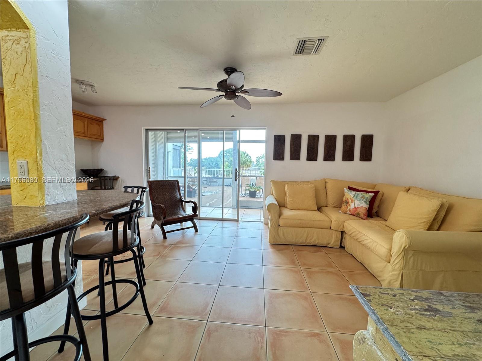 A living room features tile floors, a yellow sectional sofa, and a sliding glass door — 1700 Pierce St # 202, Hollywood FL 33020, HOLLYWOOD, FL
