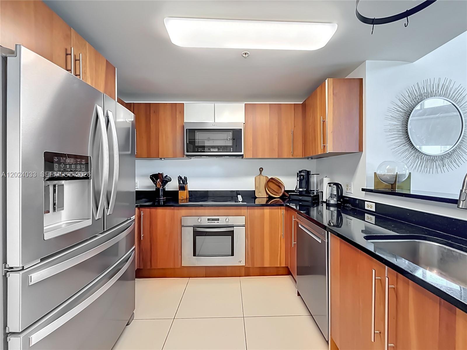 A kitchen features wood cabinets, stainless steel appliances, and black countertops — 300 S Biscayne Blvd # 1016, Miami FL 33131, MIAMI, FL
