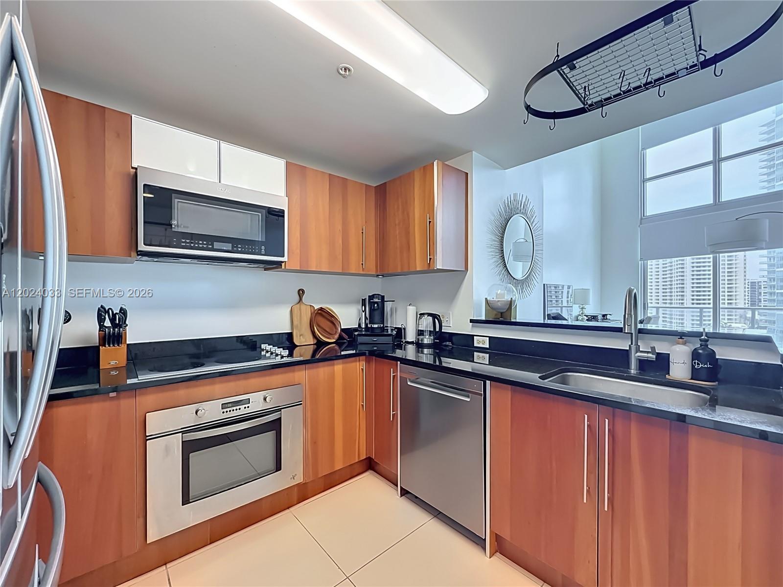 A kitchen features wood cabinets, black countertops, stainless steel appliances, and a pass-through window — 300 S Biscayne Blvd # 1016, Miami FL 33131, MIAMI, FL