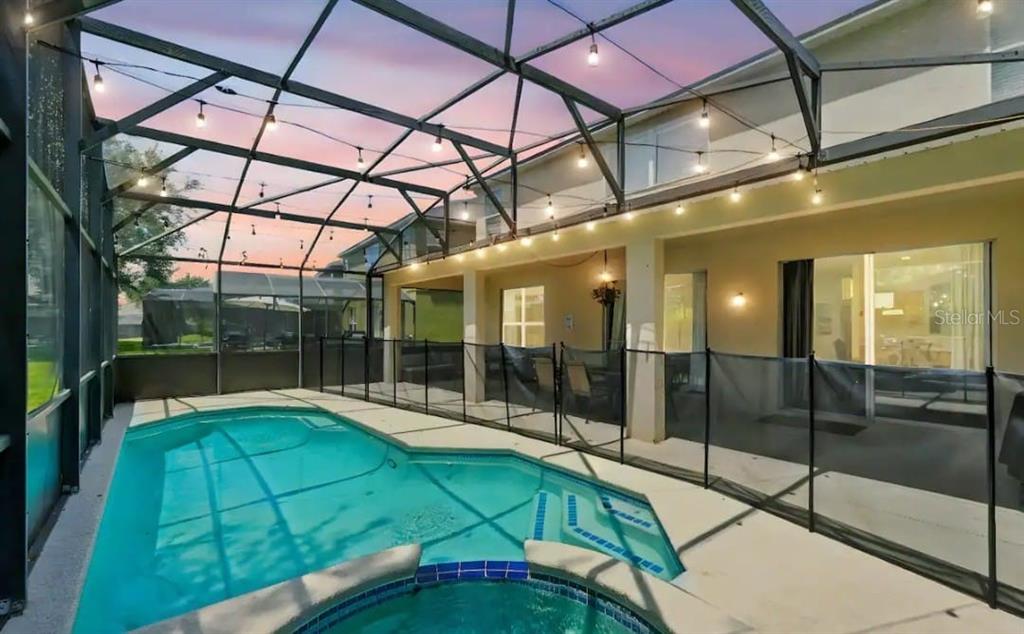 A screened-in patio features a swimming pool, a hot tub, and string lights at dusk — 8520 SUNRISE KEY DRIVE, KISSIMMEE, FL