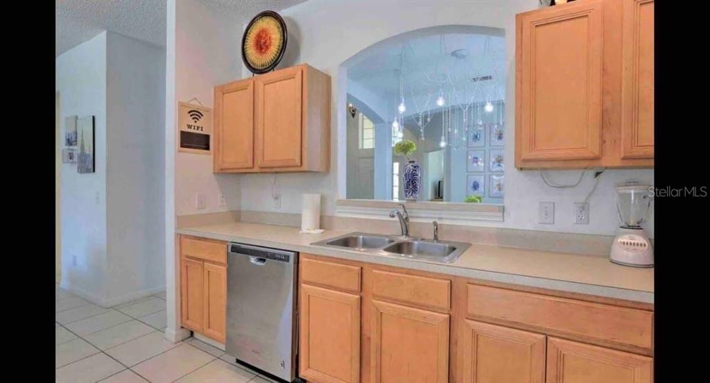 A kitchen features light wood cabinets, a stainless steel dishwasher, and a pass-through window — 8520 SUNRISE KEY DRIVE, KISSIMMEE, FL