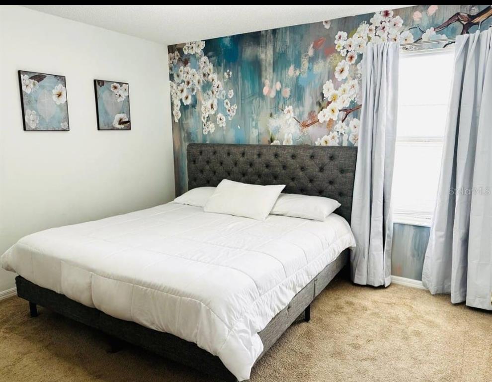 A bedroom features a tufted gray bed against a floral mural accent wall — 8520 SUNRISE KEY DRIVE, KISSIMMEE, FL