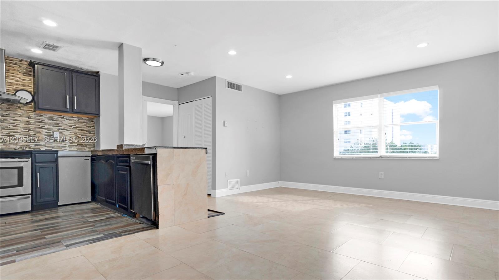 An open-concept kitchen with dark cabinets and a breakfast bar connects to a living area — 7925 Carlyle Ave # 403, Miami Beach FL 33141, MIAMI BEACH, FL