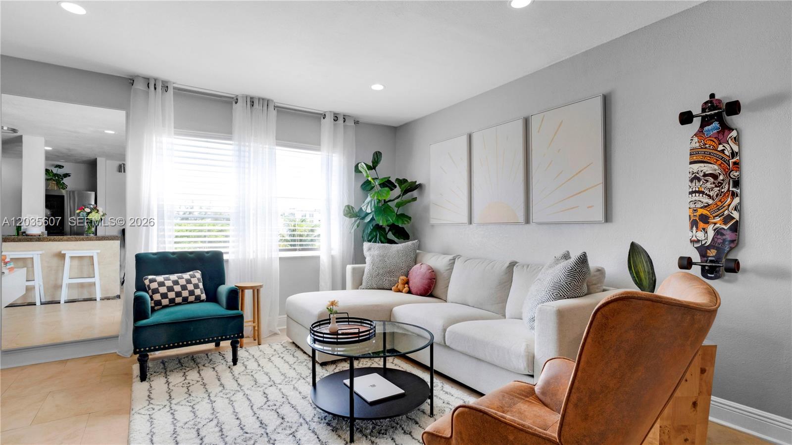 A living room features a white sectional sofa, a teal armchair, and a wall-mounted skateboard — 7925 Carlyle Ave # 403, Miami Beach FL 33141, MIAMI BEACH, FL