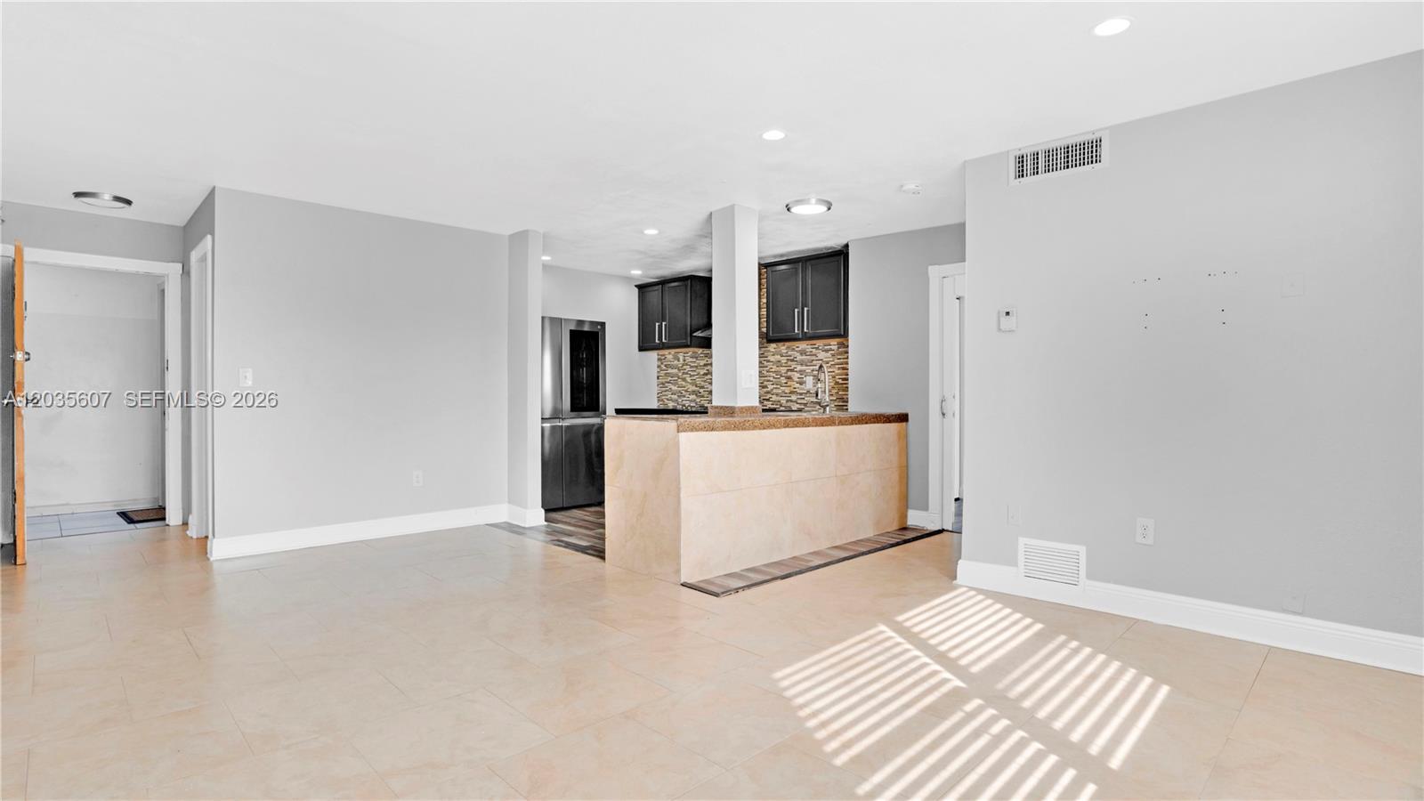 An open-concept kitchen features dark cabinets, a tiled breakfast bar, and light-colored floor tiles — 7925 Carlyle Ave # 403, Miami Beach FL 33141, MIAMI BEACH, FL