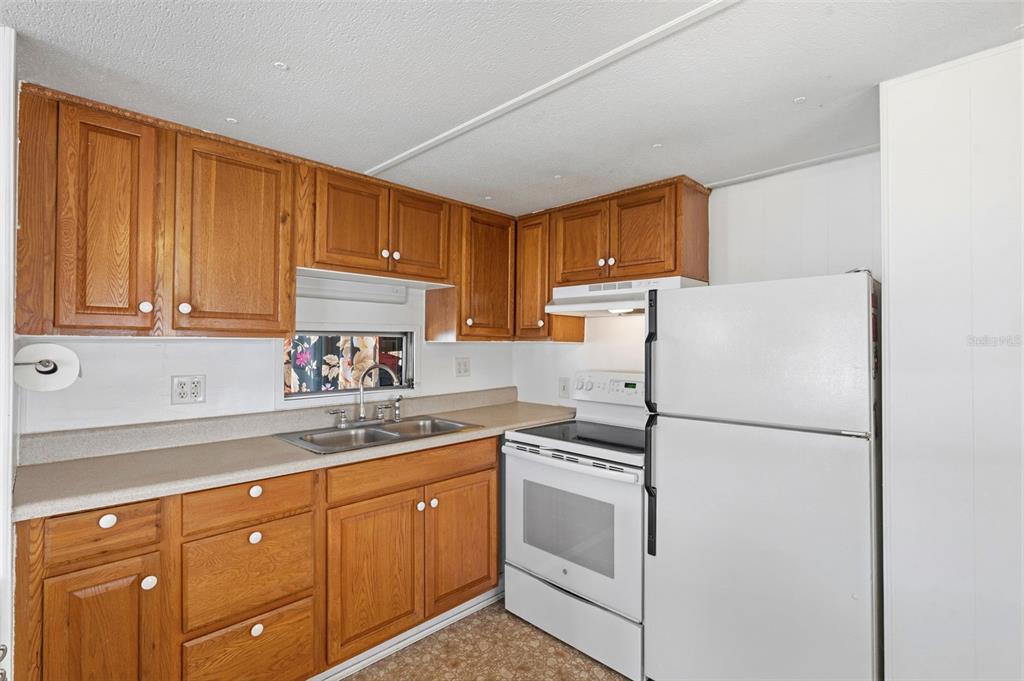A kitchen features wood cabinets, a white stove, a white refrigerator, and a double sink — 4687 67TH STREET N UNIT 23, ST PETERSBURG, FL