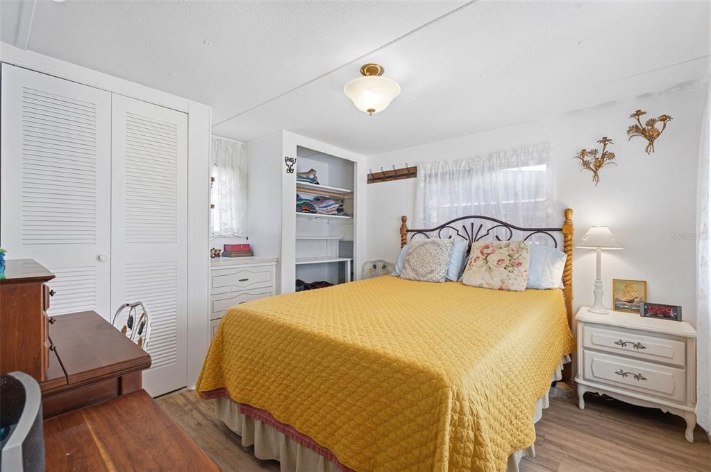 A bedroom features a yellow quilt on the bed, white louvered closet doors, and open shelving — 4687 67TH STREET N UNIT 23, ST PETERSBURG, FL
