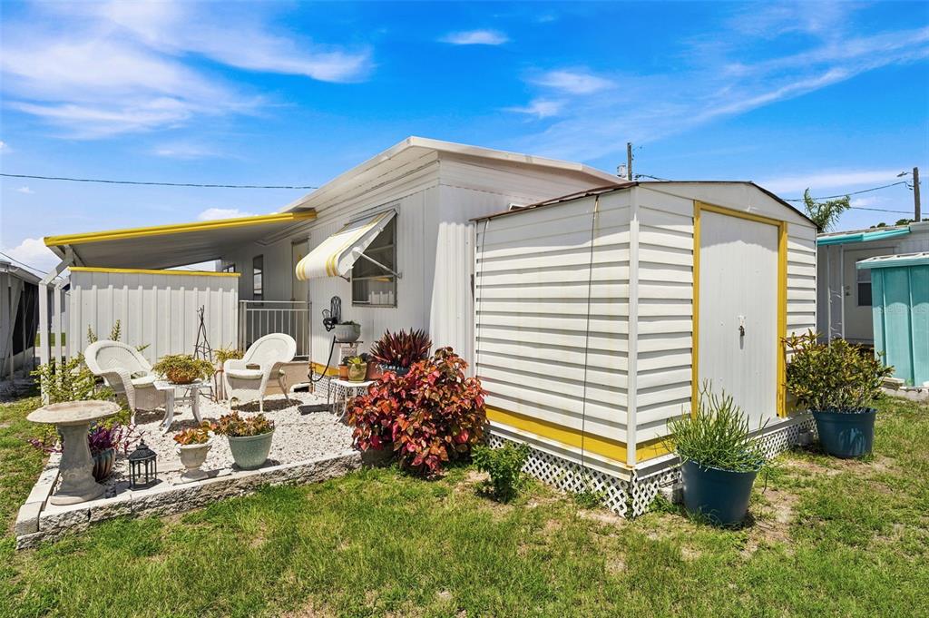 A mobile home exterior features a gravel patio, white siding, a storage shed, and landscaping — 4687 67TH STREET N UNIT 23, ST PETERSBURG, FL