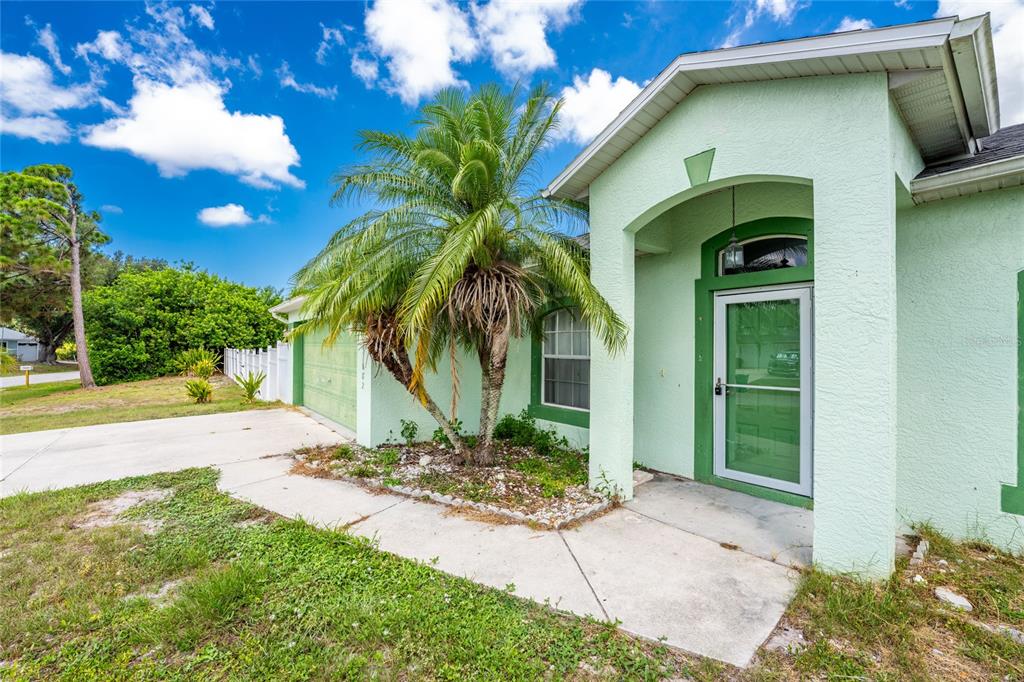 A light green house exterior features a palm tree, a concrete walkway, and a front door — 11082 VANESSA AVENUE, ENGLEWOOD, FL