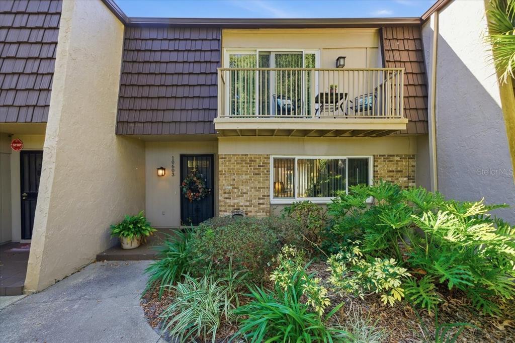 A two-story townhouse exterior features a brick facade, a second-floor balcony, and landscaped front garden — 10603 CARROLLBROOK WAY UNIT 10603, TAMPA, FL
