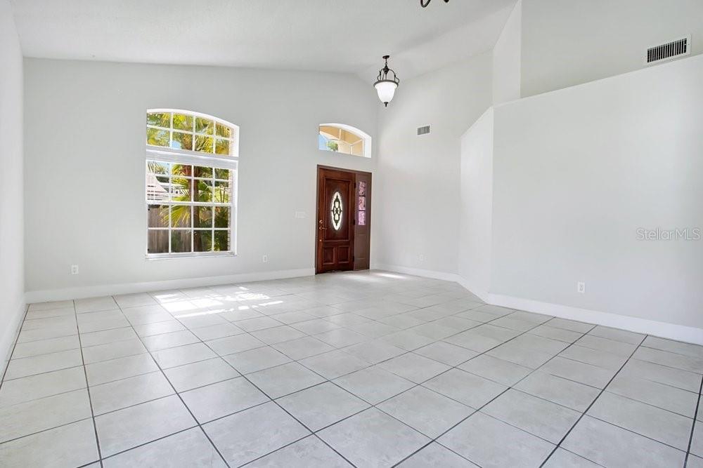 A bright, empty foyer features white walls, light-colored tile flooring, and a wooden front door — 3127 BIRMINGHAM BOULEVARD, ORLANDO, FL