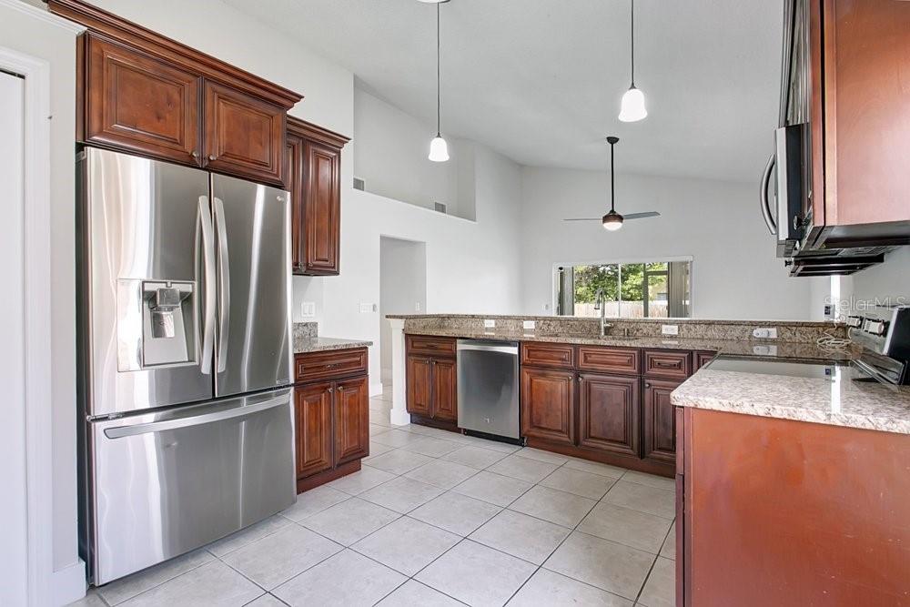 A kitchen features dark wood cabinets, stainless steel appliances, and granite countertops with tile flooring — 3127 BIRMINGHAM BOULEVARD, ORLANDO, FL