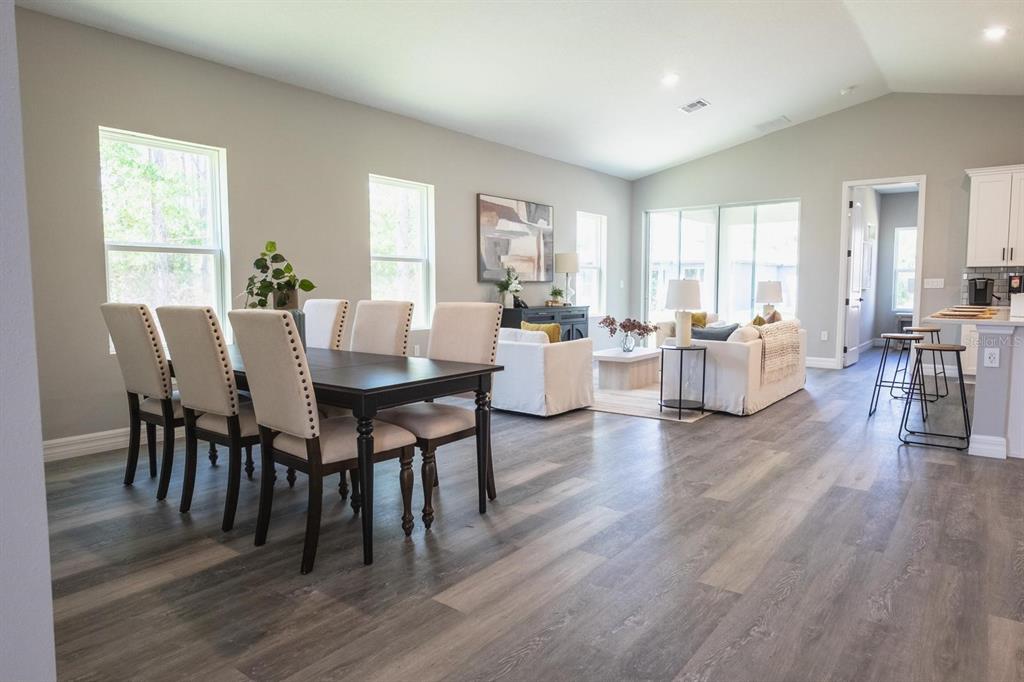 An open-concept living and dining area features wood-look flooring, neutral walls, and large windows — 2424 SW 159 LANE, OCALA, FL