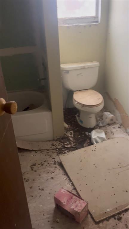 A bathroom with a white toilet, a bathtub, and significant debris scattered across the floor — 44750 MISTY ISLE DRIVE, DELAND, FL