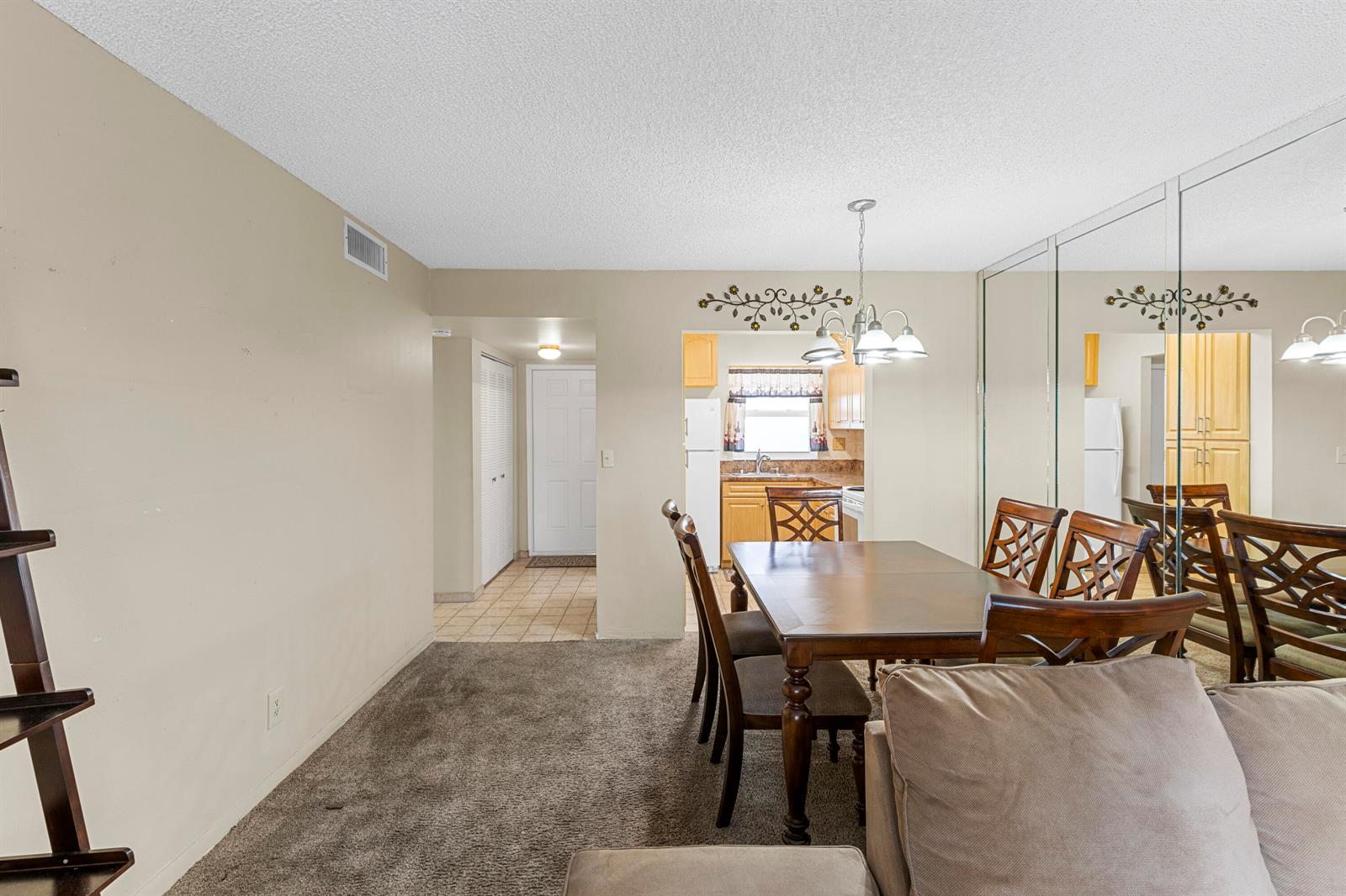 A dining area with a wooden table, chairs, and a mirrored wall next to a kitchen — SUNRISE, FL