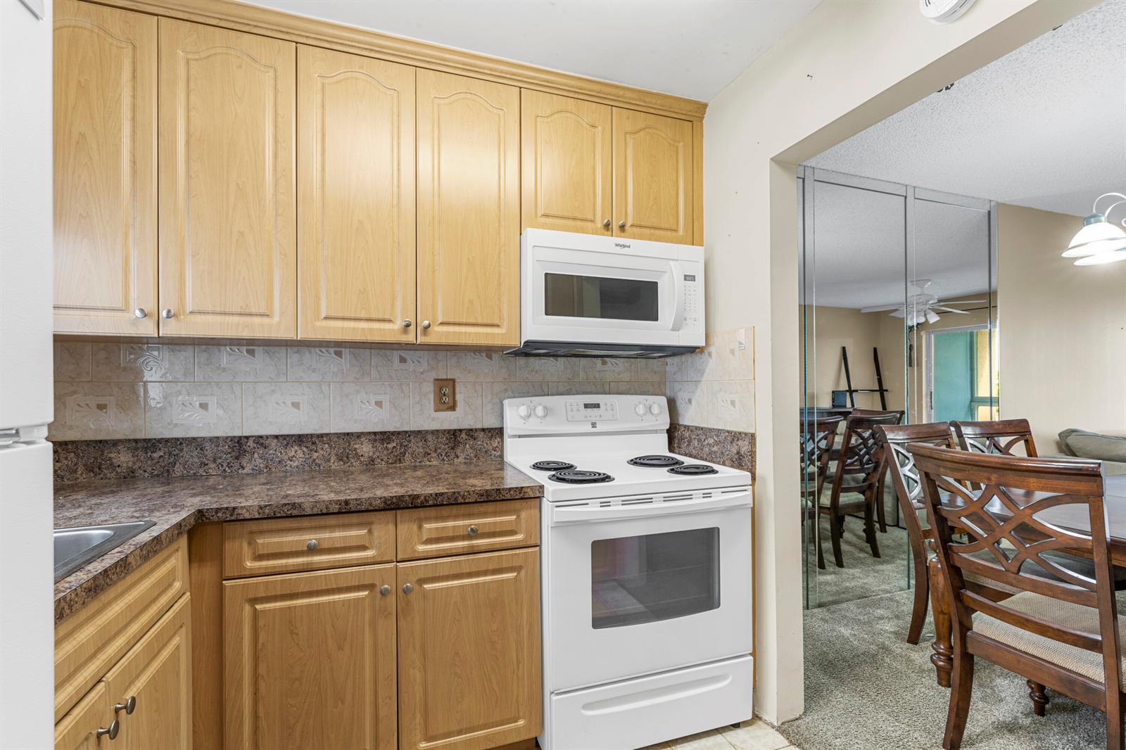 A kitchen features light wood cabinets, dark laminate countertops, and white appliances — SUNRISE, FL
