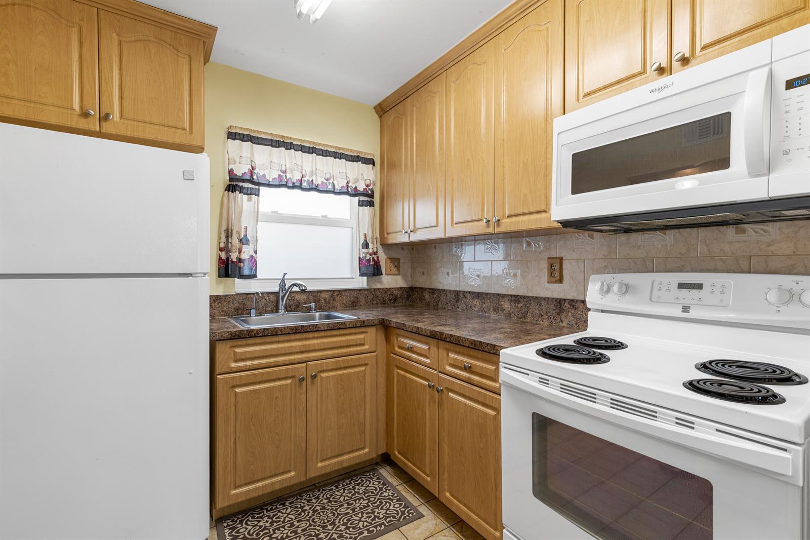 A kitchen features light wood cabinets, white appliances, a window with a valance, and countertops — SUNRISE, FL