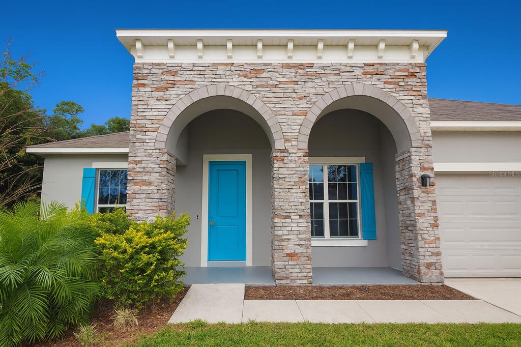 A house exterior features a stone-faced arched entryway, a bright blue door, and blue shutters — 26047 EXMOOR DRIVE, SORRENTO, FL