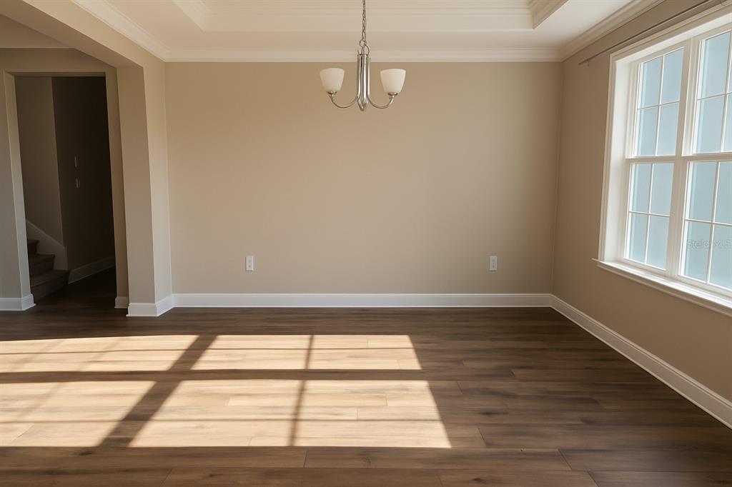 An empty dining room features light beige walls, wood-look flooring, and a central chandelier — 26047 EXMOOR DRIVE, SORRENTO, FL