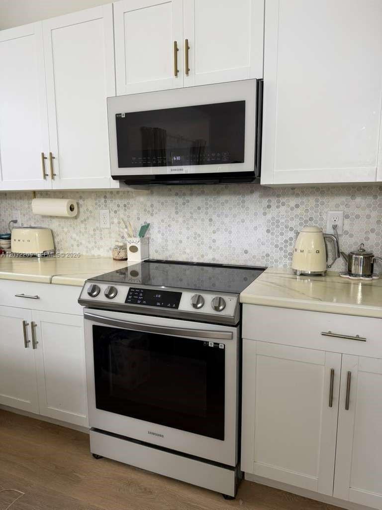 A kitchen features white cabinets, a stainless steel microwave, a glass-top stove, and tiled backsplash — 20731 NE 7th Pl # 20731, Miami FL 33179, MIAMI, FL