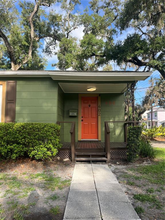 A green house exterior features a bright orange front door and a small wooden porch — 402 W PARIS STREET, TAMPA, FL