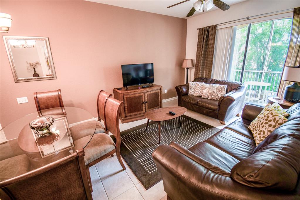 A living and dining area features a glass table, leather sofas, and a television console — 2788 ALMATON LOOP UNIT 202, KISSIMMEE, FL
