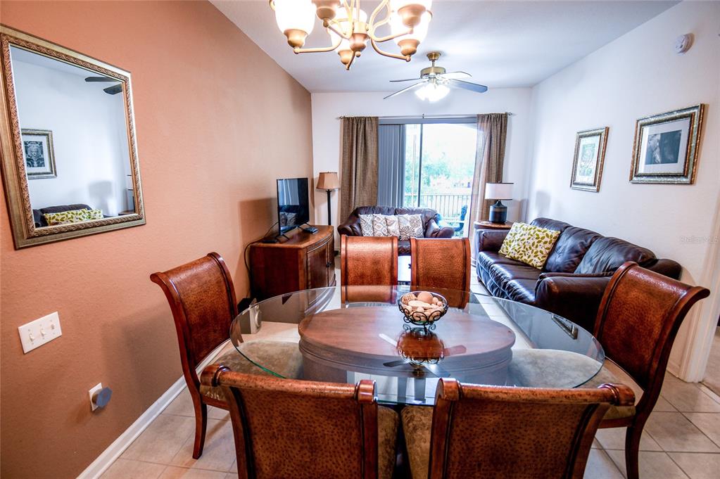 A dining area with a glass-topped table and chairs opens into a living room — 2788 ALMATON LOOP UNIT 202, KISSIMMEE, FL
