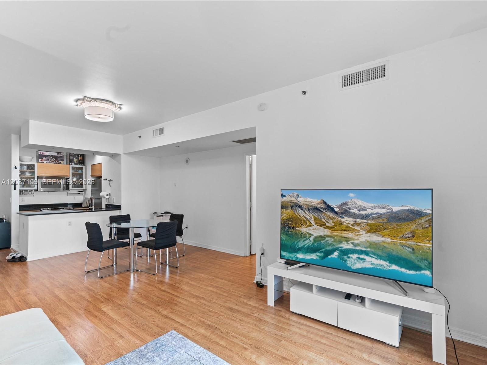 A living room with wood flooring features a television on a white stand and an adjacent kitchen — 950 Brickell Bay Dr # 501, Miami FL 33131, MIAMI, FL