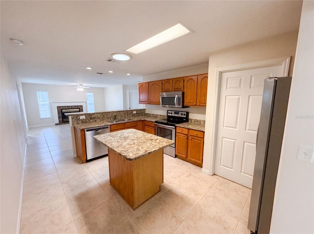 A kitchen with wood cabinets, granite countertops, and an island overlooks a living room — 1015 DEER RUN DRIVE, MELBOURNE, FL
