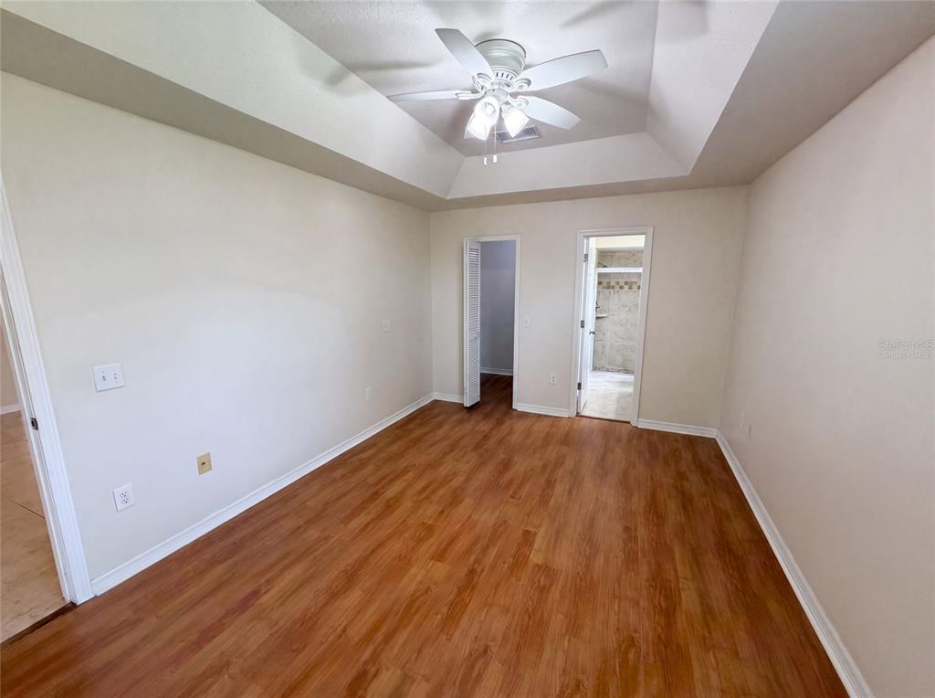 An empty bedroom features wood-look flooring, a tray ceiling with a fan, and two doorways — 1015 DEER RUN DRIVE, MELBOURNE, FL