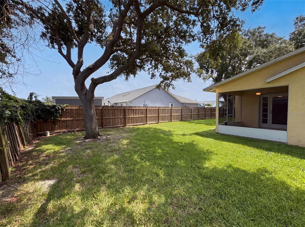 A grassy backyard features a large tree, a wooden fence, and a screened-in patio — 1015 DEER RUN DRIVE, MELBOURNE, FL
