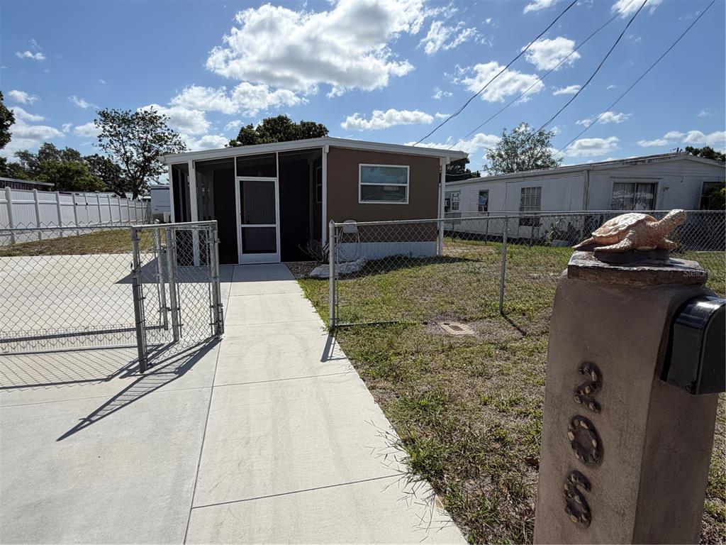 A brown mobile home with a screened porch sits behind a chain-link fence — 206 RAVENNA STREET N, NOKOMIS, FL