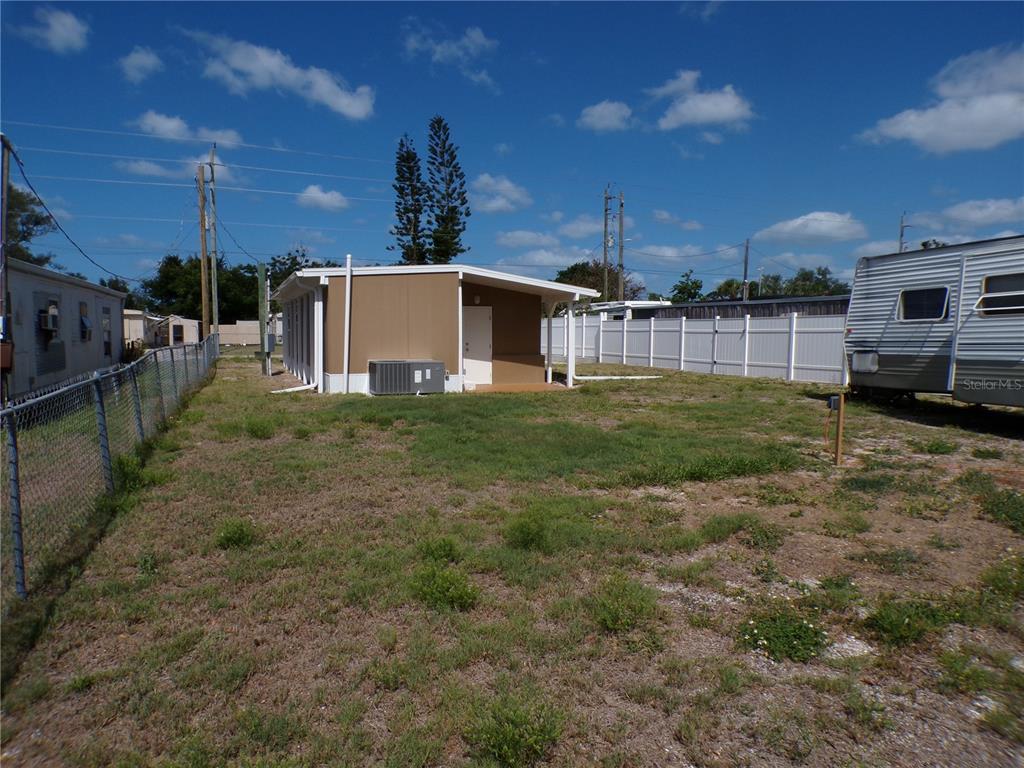 A tan mobile home sits on a grassy lot next to a white fence — 206 RAVENNA STREET N, NOKOMIS, FL