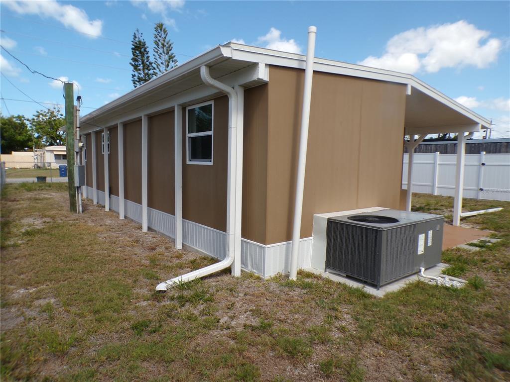 The exterior side of a tan mobile home features a white gutter system and HVAC unit — 206 RAVENNA STREET N, NOKOMIS, FL